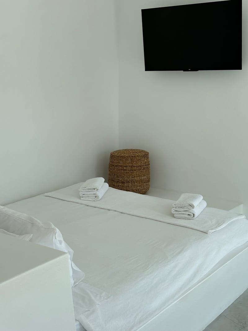 Bed made up with white linen and towels, a woven basket and the wall-mounted TV
