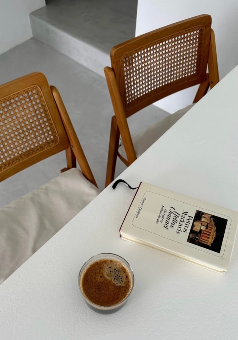 Δύο ψάθινες καρέκλες, ένας καφές και ένα βιβλίο στον πάγκο του πρωινού